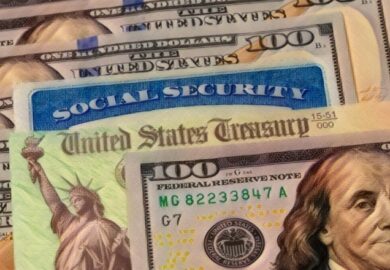 social security card lays among 100 dollar bills and a treasury note showing the budget proposal