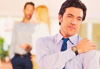Man at work suffering from shoulder pain with co-workers in the background.