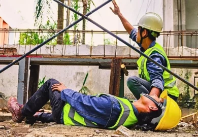 An injured worker holding his hurt knee with his co-worker asking for help.