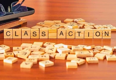 Class action word spelled on scrabble tiles on a wooden table with glasses and a book.