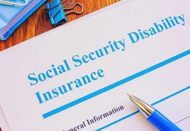 Social Security Disability Insurance application form with pen on top and notebook and clips on the desk.