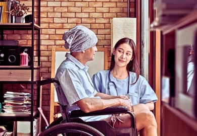 Elderly patient in wheelchair with nurse beside him.