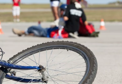 Bicycle tire on the front with paramedics aiding the injured pedestrian on the background.